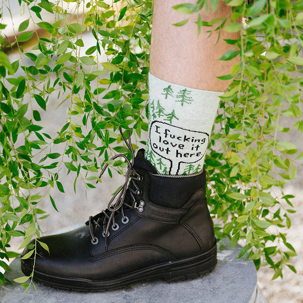 A man wearing nature socks that say "I fucking love it out here" next to green plants