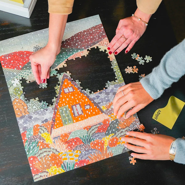 Hands putting together a puzzle of a snowy cabin in the woods
