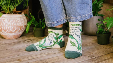 a woman wearing plants get me crazy novelty socks by blue q while watering plants