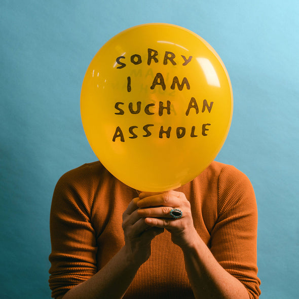 A woman holding a balloon that says, "Sorry I am such an asshole"
