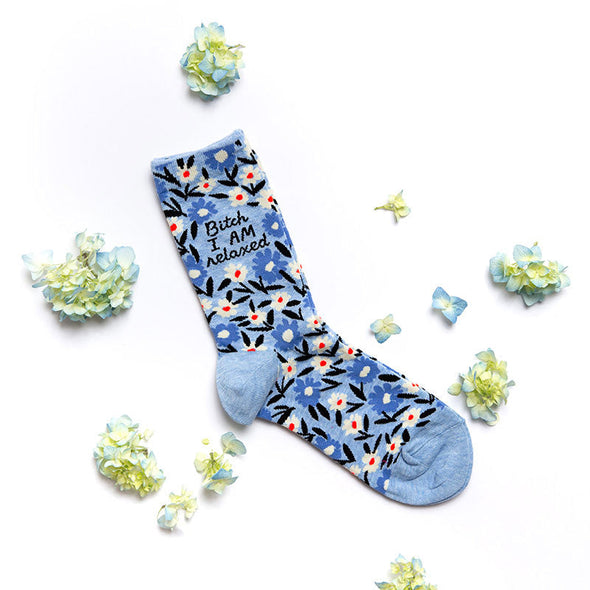 Funny floral socks for women that say, “Bitch, I AM relaxed” laying flat next to flowers