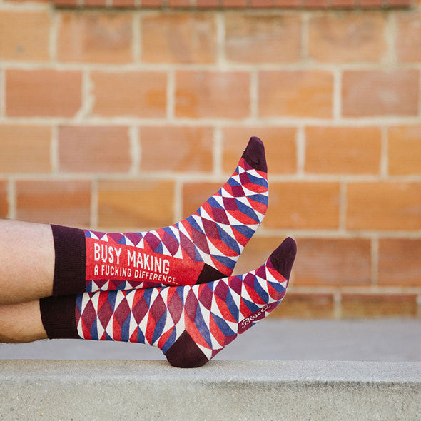 A man wearing funny socks that say, "Busy making a fucking difference"