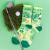 golf club, golf ball and a patch of green grass next to funny men's socks that say, "I'm a golf guy. BIG golf guy."