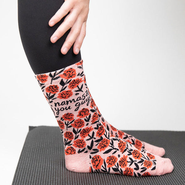woman standing on a yoga mat wearing cute socks with a flower pattern and the words "namaste you guys"