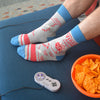 man wearing video game socks with a game controller and a bowl of chips nearby