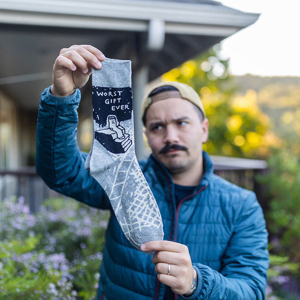 frowning man holding up funny socks that say, "worst gift ever"