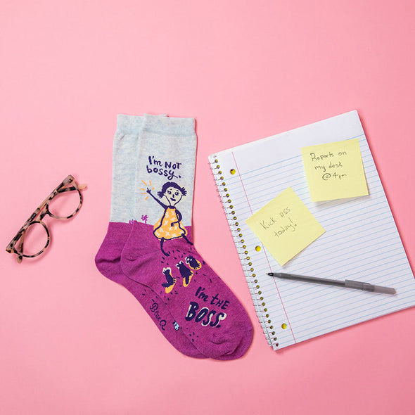 cute women's socks that say, "I'm not bossy, I'm the boss" alongside glasses, a spiral notebook and sticky notes
