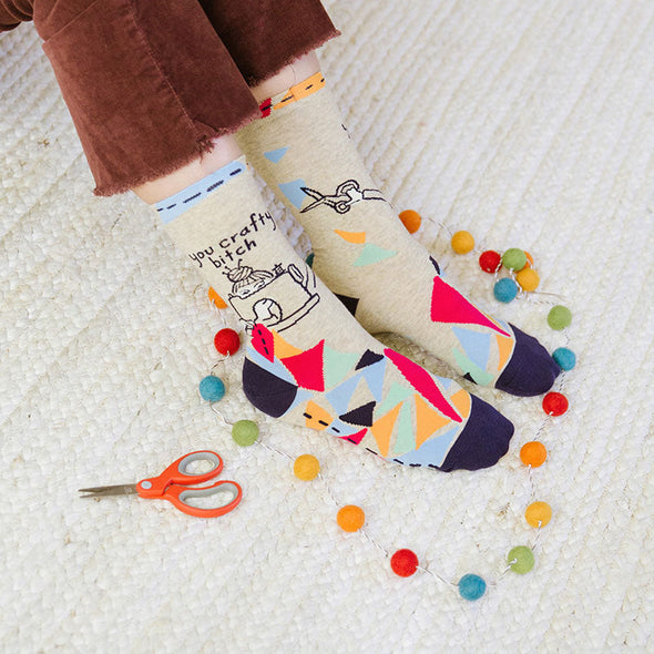 A woman wearing funny socks that say “you crafty bitch”