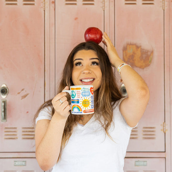 young woman with an apple on her head, holding a coffee mug full of positive sayings