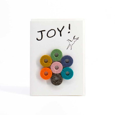 Colorful, round felt wine charms with a card that says, “Joy!”