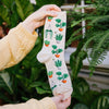 A woman holding a pair of socks with a pattern of green potted plants