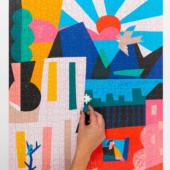 Hand putting together a puzzle of a cubist scene of a city and mountains