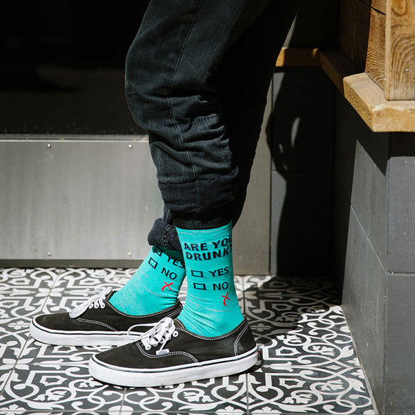Man wearing funny men's socks that say "Are you drunk?" with boxes to check "Yes" or "No" and a check mark that missed both boxes