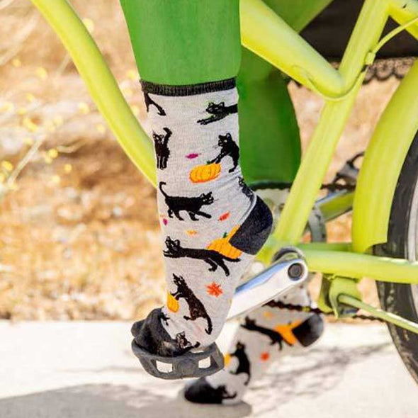 witch riding a bicycle and wearing fun Halloween socks with back cats and orange pumpkins