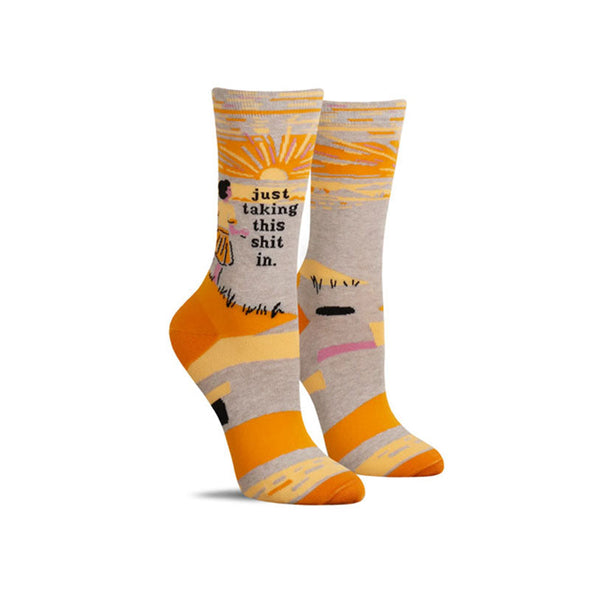 Funny women’s socks with a woman watching a sunset and the words “just taking this shit in”