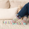 Woman sitting on a couch and wearing cute women's socks with colorful stripes and the words "shhh... I'm over-thinking"