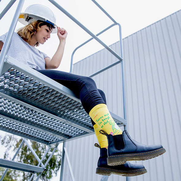 woman wearing a hard hat, jeans, boots and yellow socks that say, "turns out I'm tough as shit"