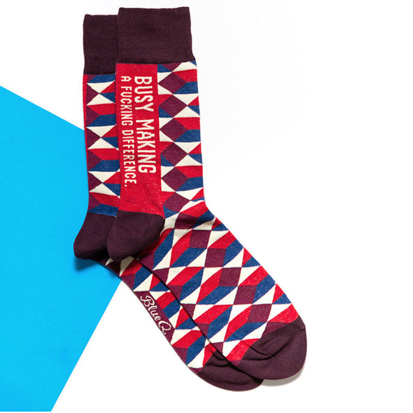 Sassy socks that say "Busy Making a Fucking Difference" laying flat