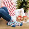 A woman sitting by a Christmas tree wearing Christmas socks in light blue with camper trailers all decorated