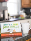 countertop with a cup of coffee and a packet of sticky notes that says "Notes for the daily struggle"