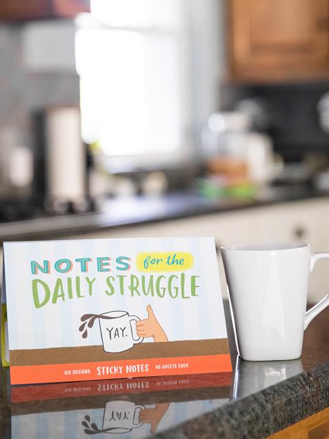 countertop with a cup of coffee and a packet of sticky notes that says "Notes for the daily struggle"