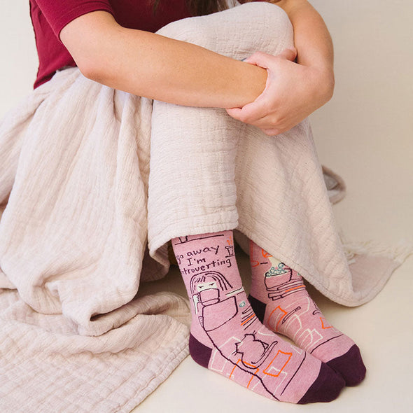 A woman wearing funny socks for women that say, “Go away, I’m introverting”