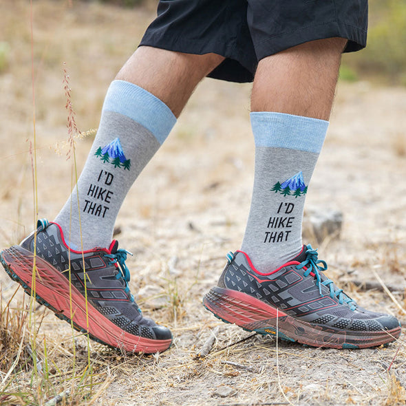 Man wearing cool hiking socks with a mountain peak, pine trees and the words “I’d hike that”
