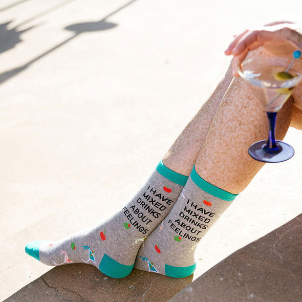 A woman wearing funny socks that say, "I have mixed drinks about feelings" while drinking a martini by a pool