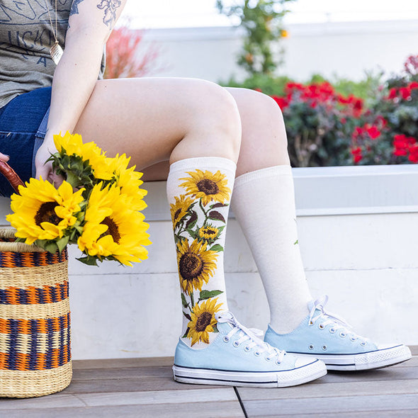 A basket of sunflowers next to a women wearing cute knee high socks with giant sunflowers on them