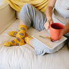 A woman wearing pancake food socks while sitting on a couch having coffee