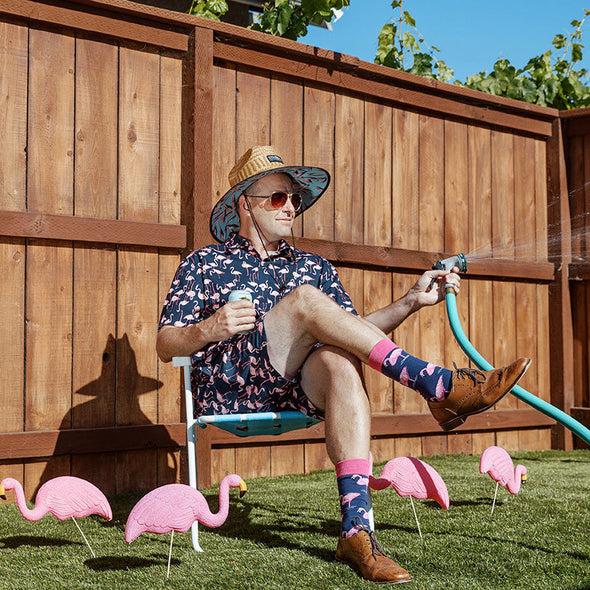 Man wearing a flamingo suit, holding a beer and a garden hose, and wearing awesome flamingo socks