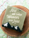 Nature socks that say "Not all who wander are lost" folded up on a wooden coaster