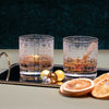 Set of two rocks glasses engraved with classic holiday sweater designs, displayed with orange garnish and cinnamon sticks